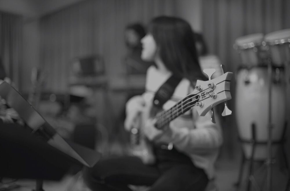 Schwarz-Weiss-Hintergrundbild einer Schülerin am E-Bass im Musikunterricht bei Maitlisek – Webdesign-Projekt von nuun gmbh, Agentur für Webdesign und UI/UX